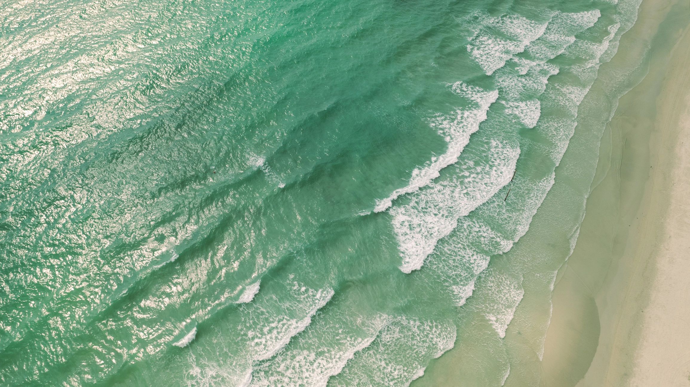 Aerial view of turquoise waves meeting a sandy beach